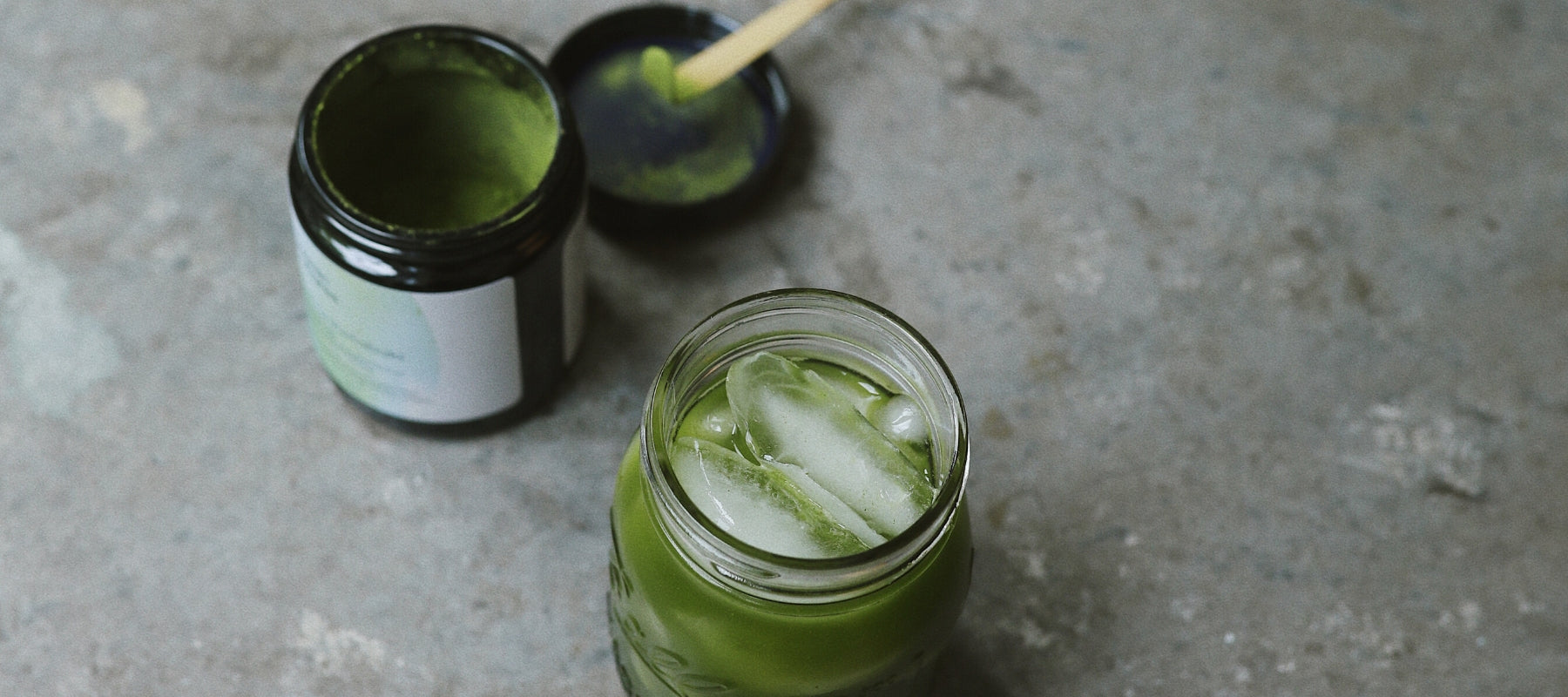 Glass of iced matcha next to a Cosmic Cultures matcha container.